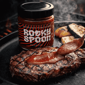 Rocky Spoon sodrus pomidorų padažas pilamas ant kepto jautienos kepsnio grilyje. Rocky Spoon rich tomato BBQ sauce poured over grilled beef steak on grill pan.